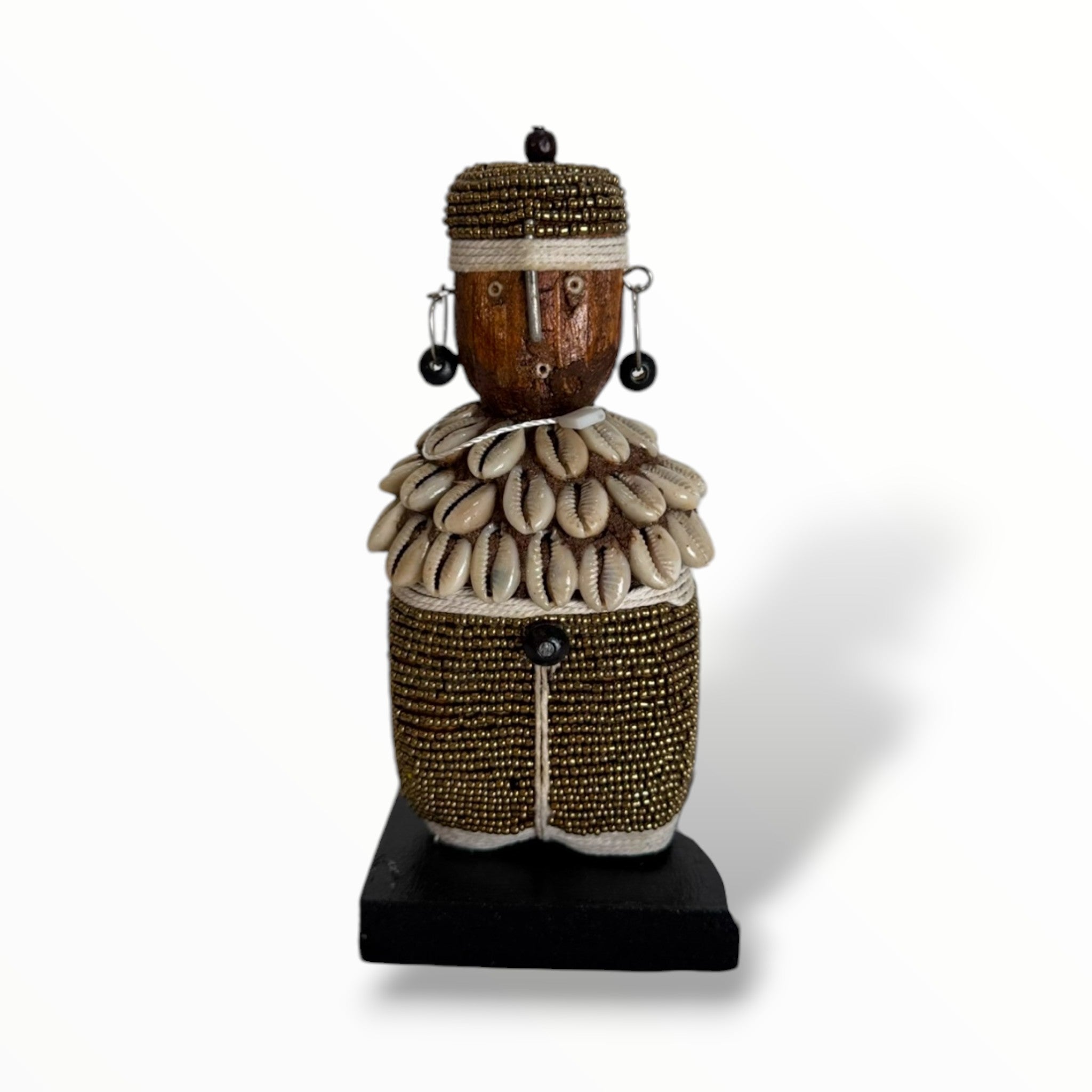 A traditional African Namji doll, made of wood and adorned with beads, cowrie shells, and metal embellishments, displayed on a white background.