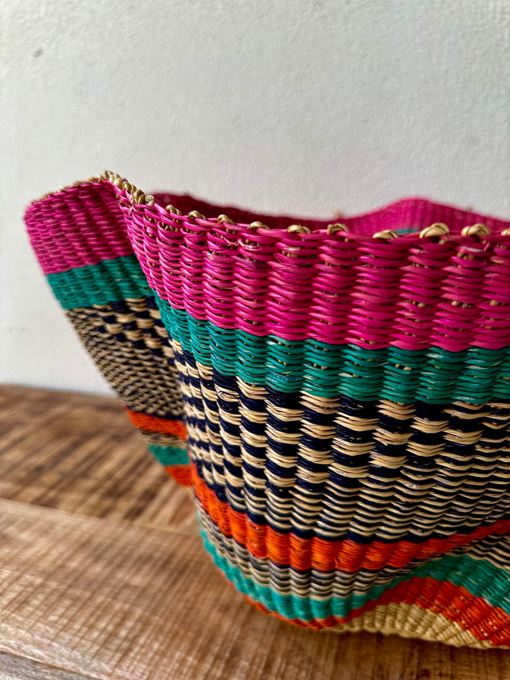 Multicolored woven basket on a wooden surface with a white background
African wavy bolga basket, Babatree basket in Dubai
