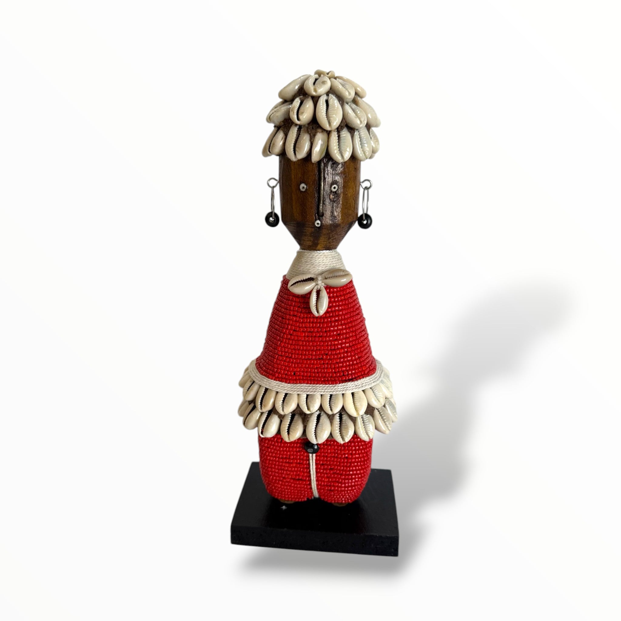 A traditional African Red Namji doll, made of wood and adorned with beads, cowrie shells, and metal embellishments, displayed on a white background.
