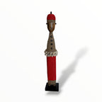 A traditional Red African Namji doll, made of wood and adorned with beads, cowrie shells, and metal embellishments, displayed on a white background.