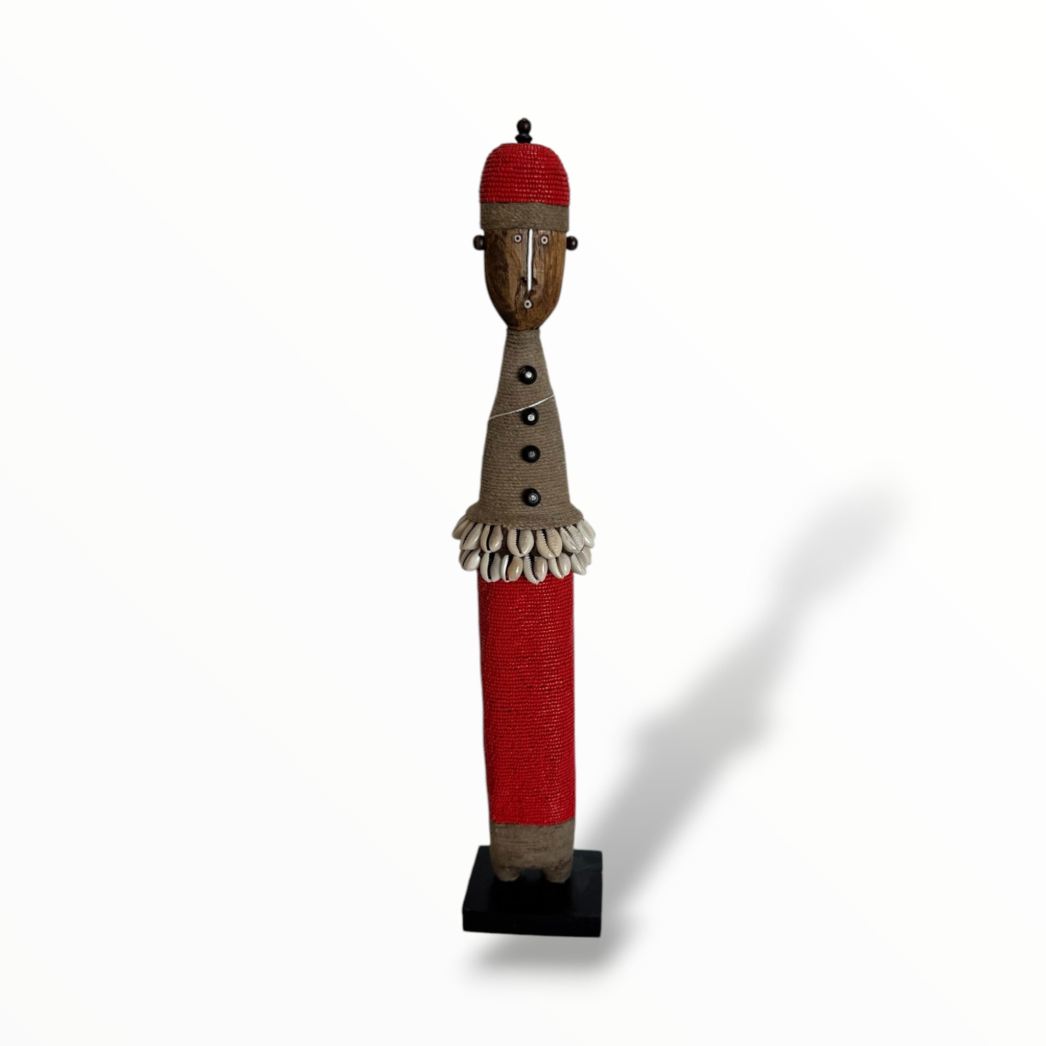 A traditional Red African Namji doll, made of wood and adorned with beads, cowrie shells, and metal embellishments, displayed on a white background.